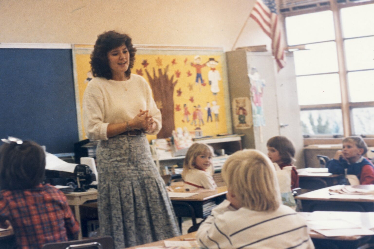 A female teacher facing her students in a classroom (flashback)