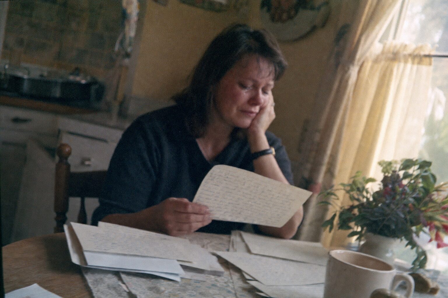 A middle-aged woman reading letters spread out on a table, one by one