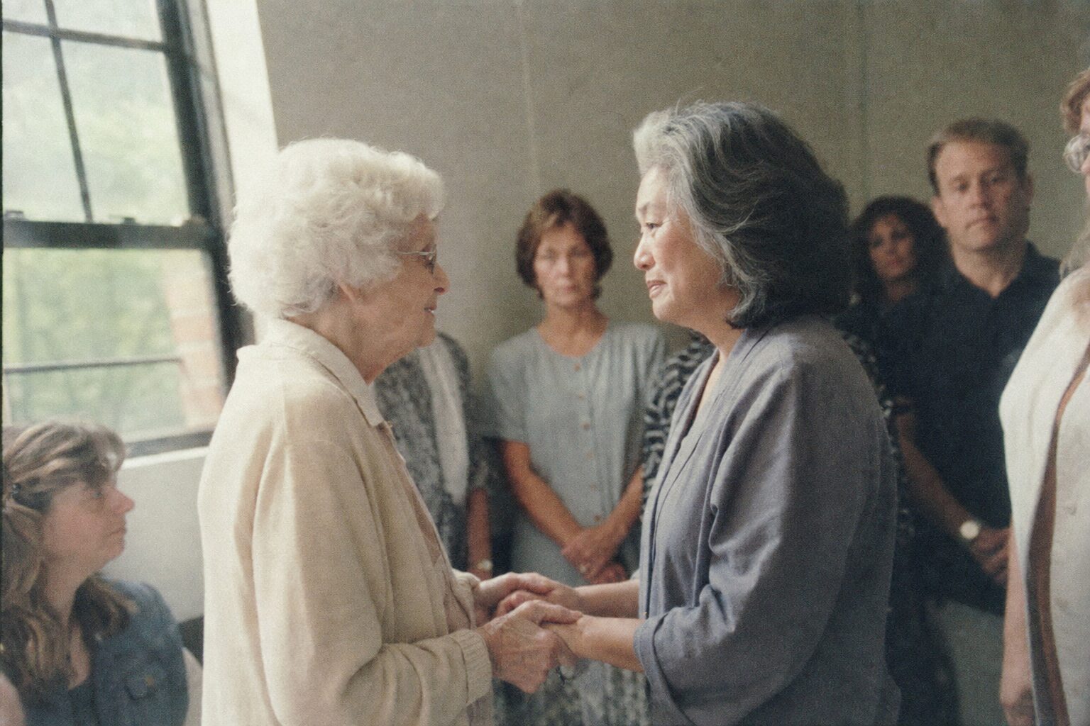 An elderly woman taking the hands of a younger woman by a window