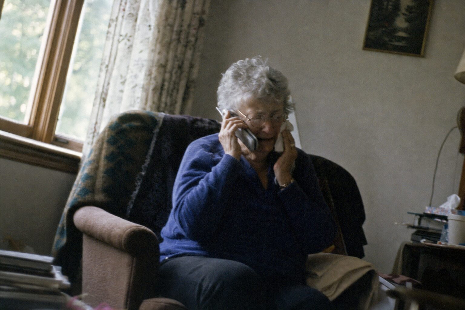 An elderly woman wiping tears while on the phone