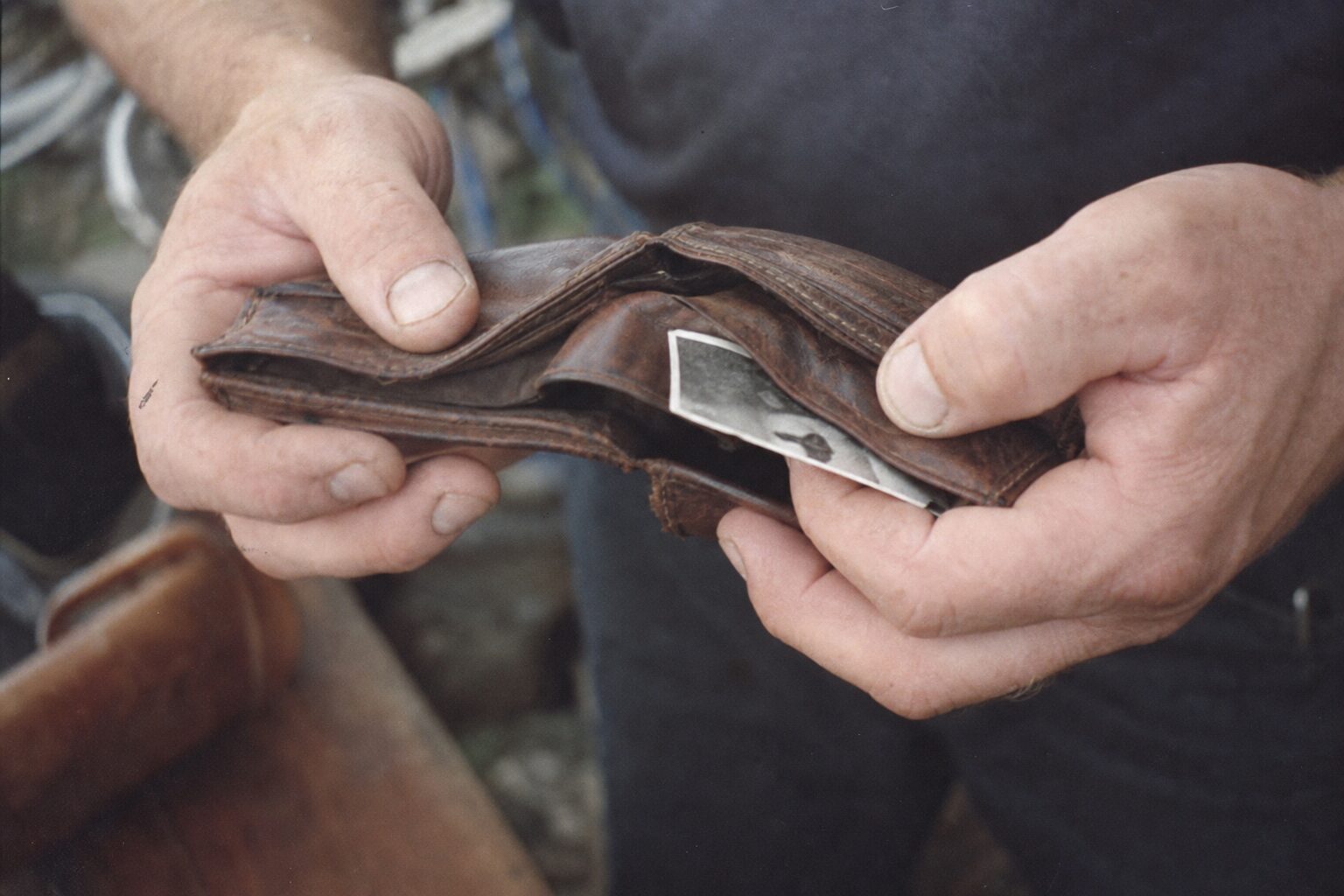 A man's hands pulling an old photograph from a worn wallet