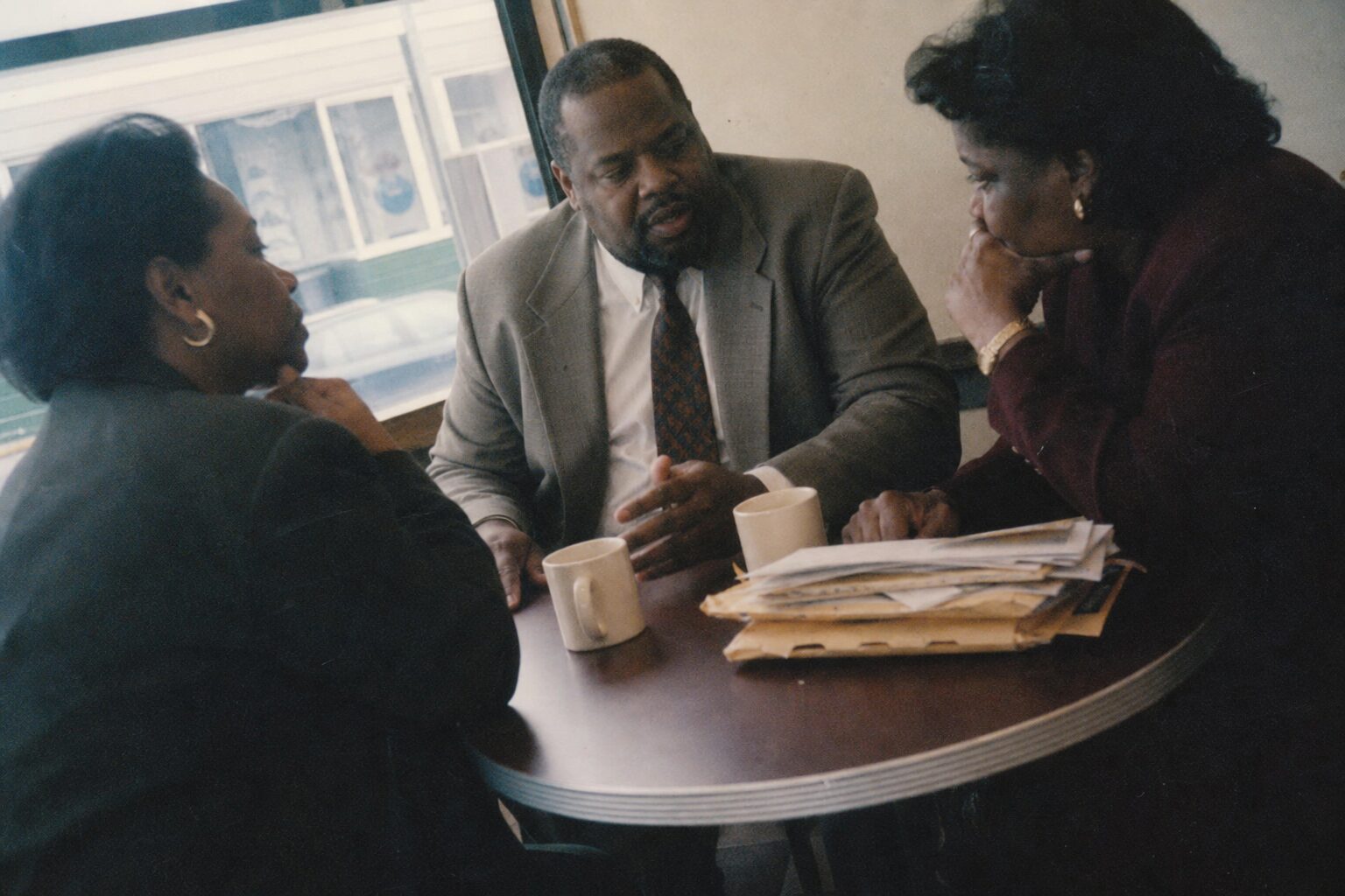 Three people sitting around a small café table in quiet conversation