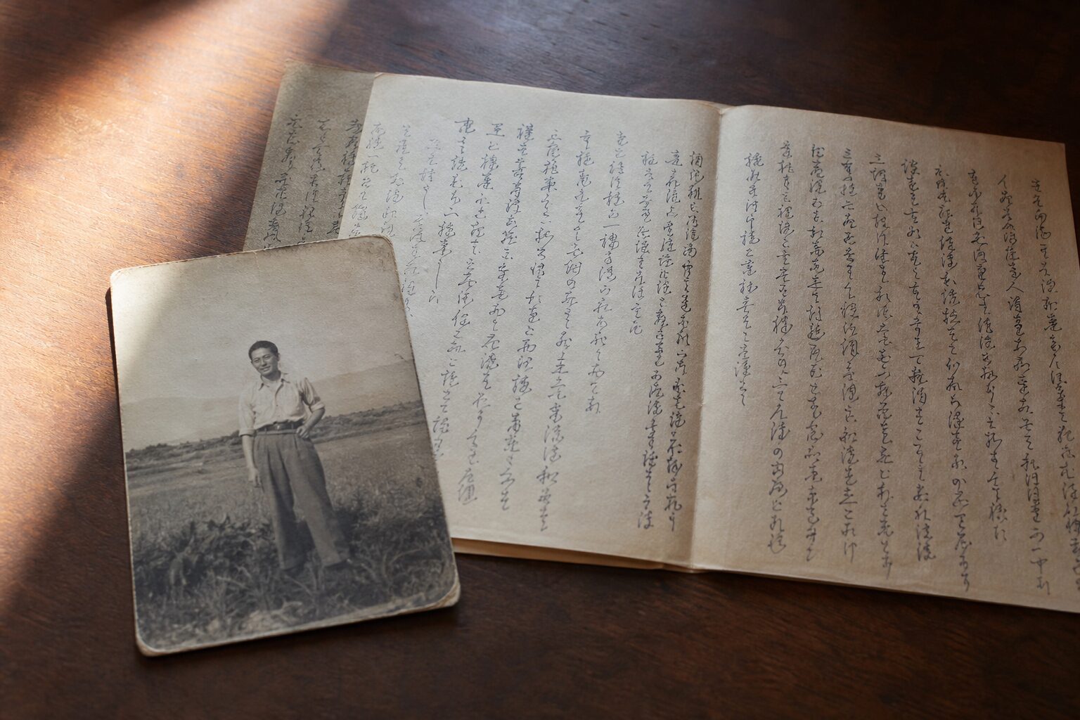 A wooden table with an old black-and-white photograph and several pages of a handwritten letter spread out in soft light